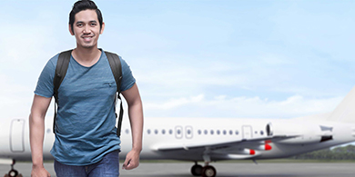 An international student walking with a plane behind him 